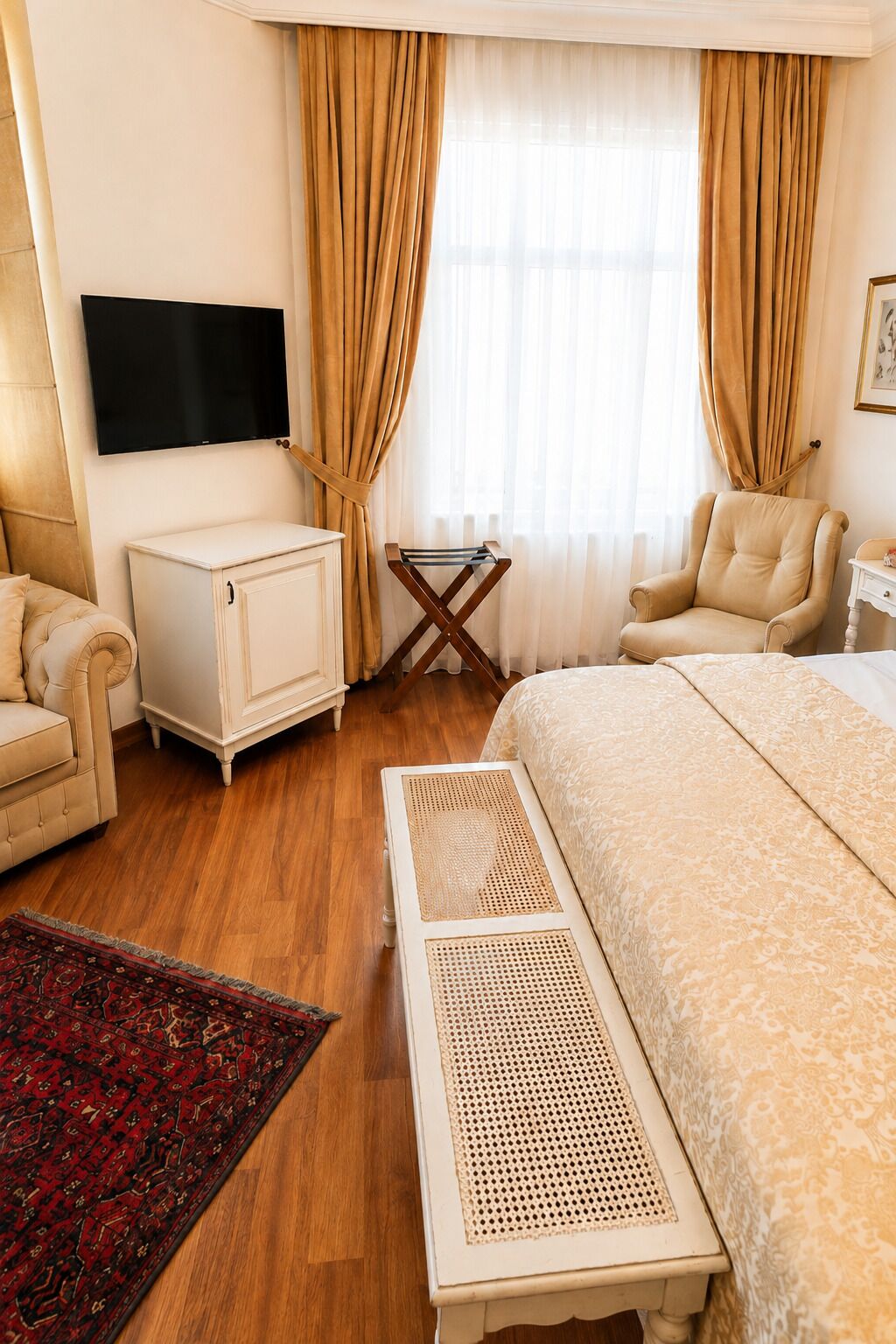A hotel room with a bed, a television, a desk, a chair, a cabinet, and a window with curtains.