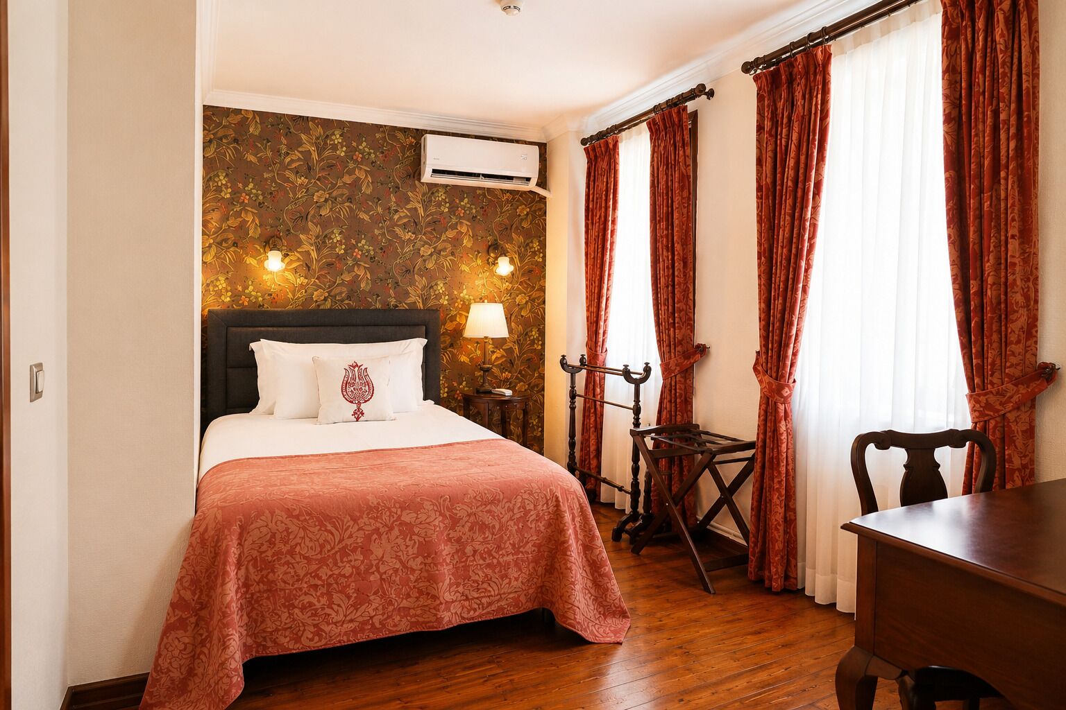 Una habitación de hotel con cama, escritorio, silla, lámpara y ventana con cortinas.