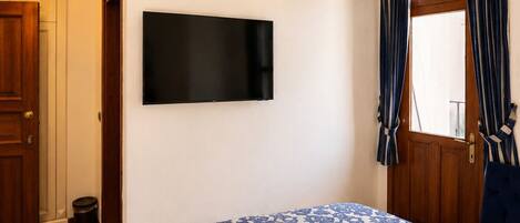 A bedroom with a bed, a mounted TV, an air conditioning unit, a window with curtains, and a door.