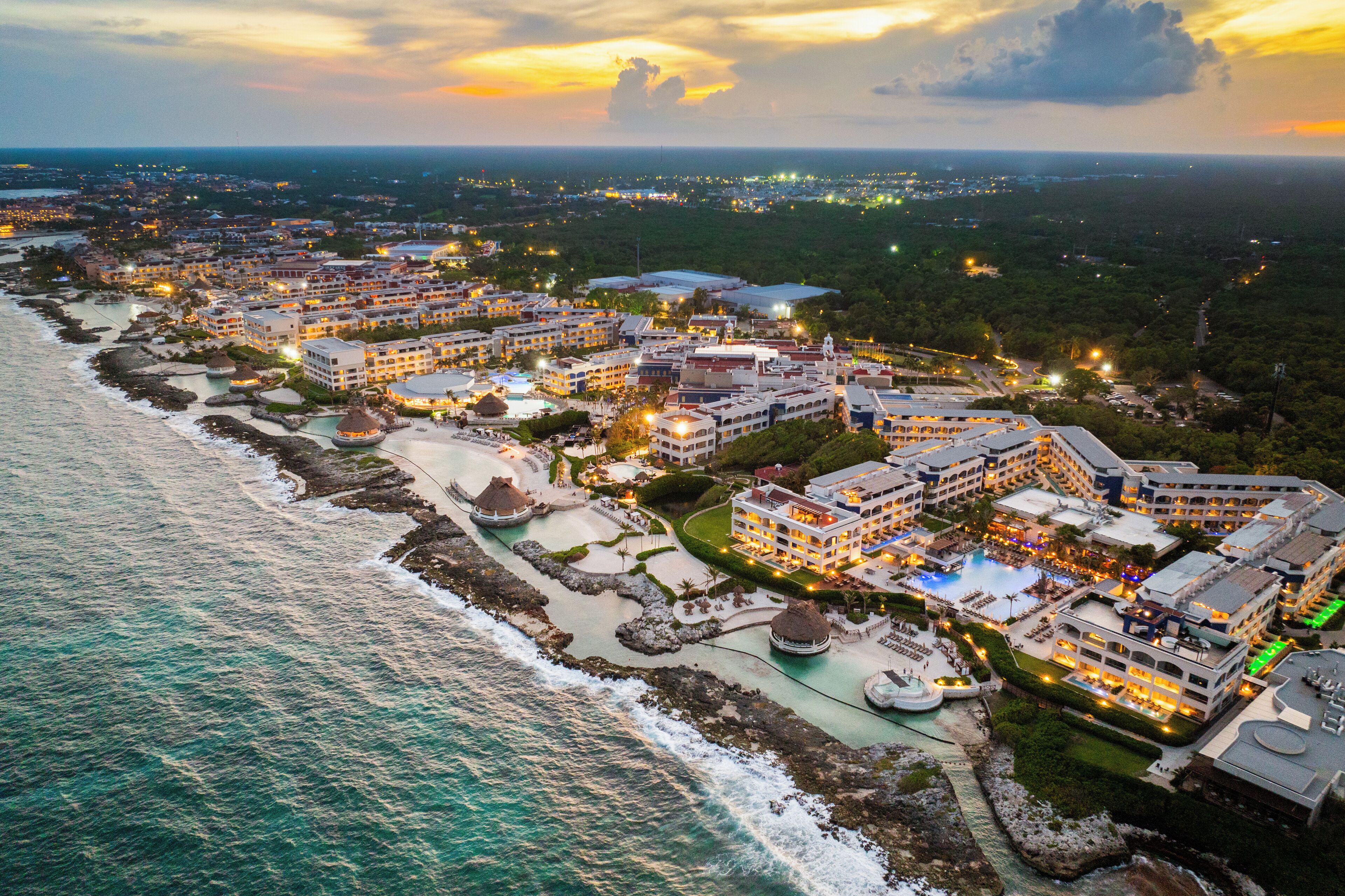 Un resort costero con varias edificaciones, frente a la playa y un área de piscina.