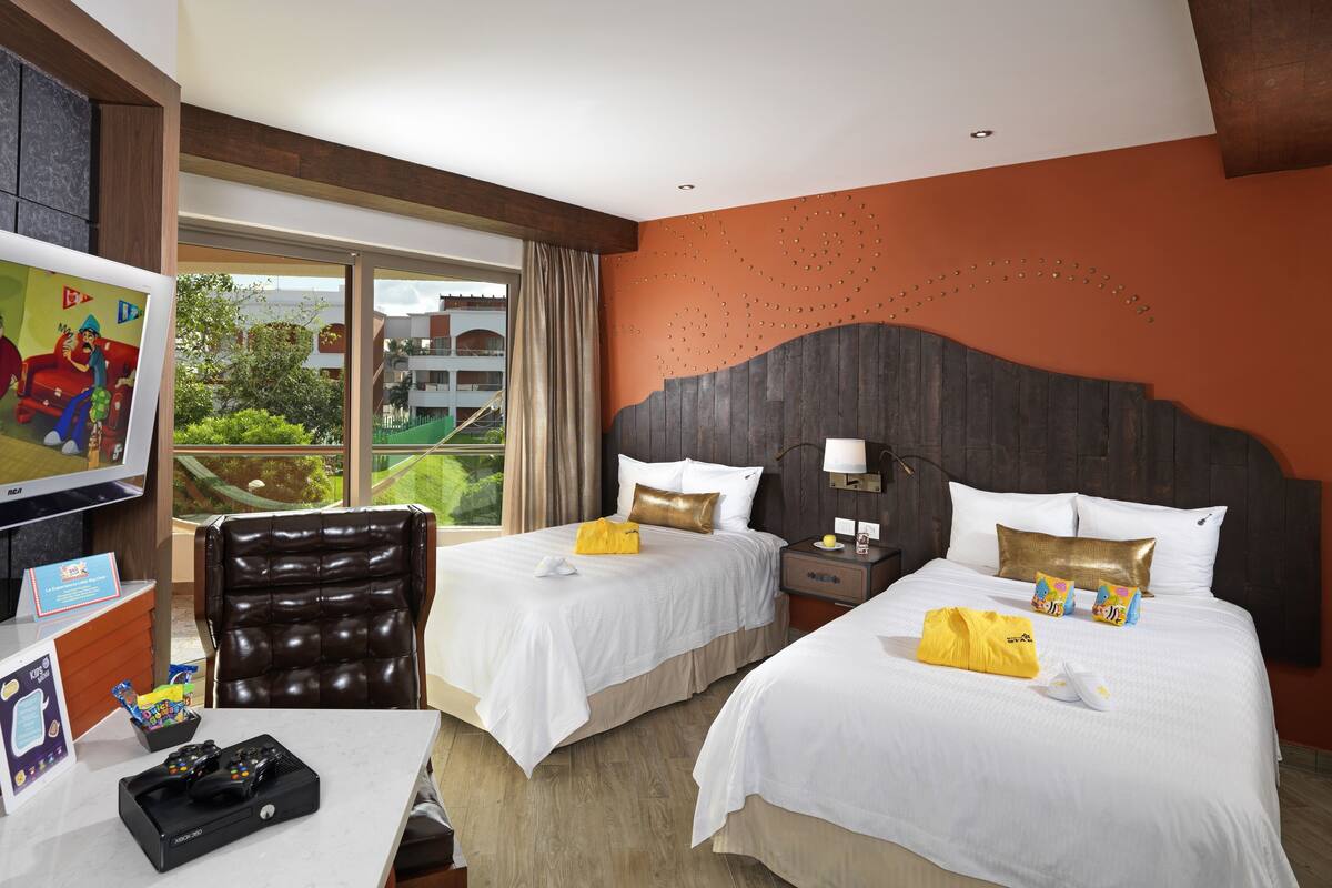 A hotel room with two beds, a desk, a TV, and a view of the outdoors.