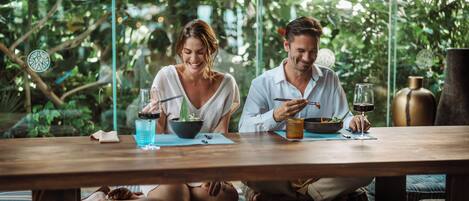 A couple dining at a wooden table with a view of lush greenery.