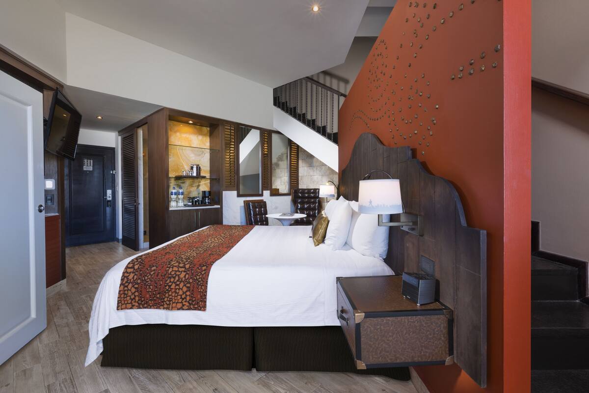 A modern hotel room with a large bed, a desk, and a staircase leading to an upper level.