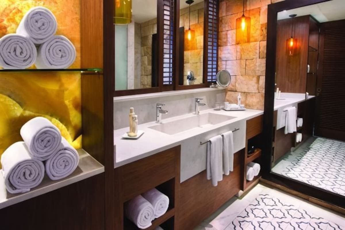 Un baño con dos lavamanos, un espejo grande y toallas en estantes.