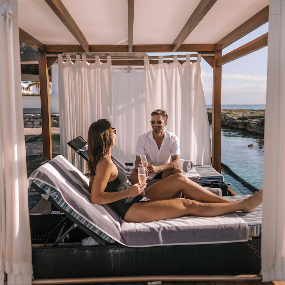 Una pareja descansando en una tumbona junto a una piscina con vista al mar.