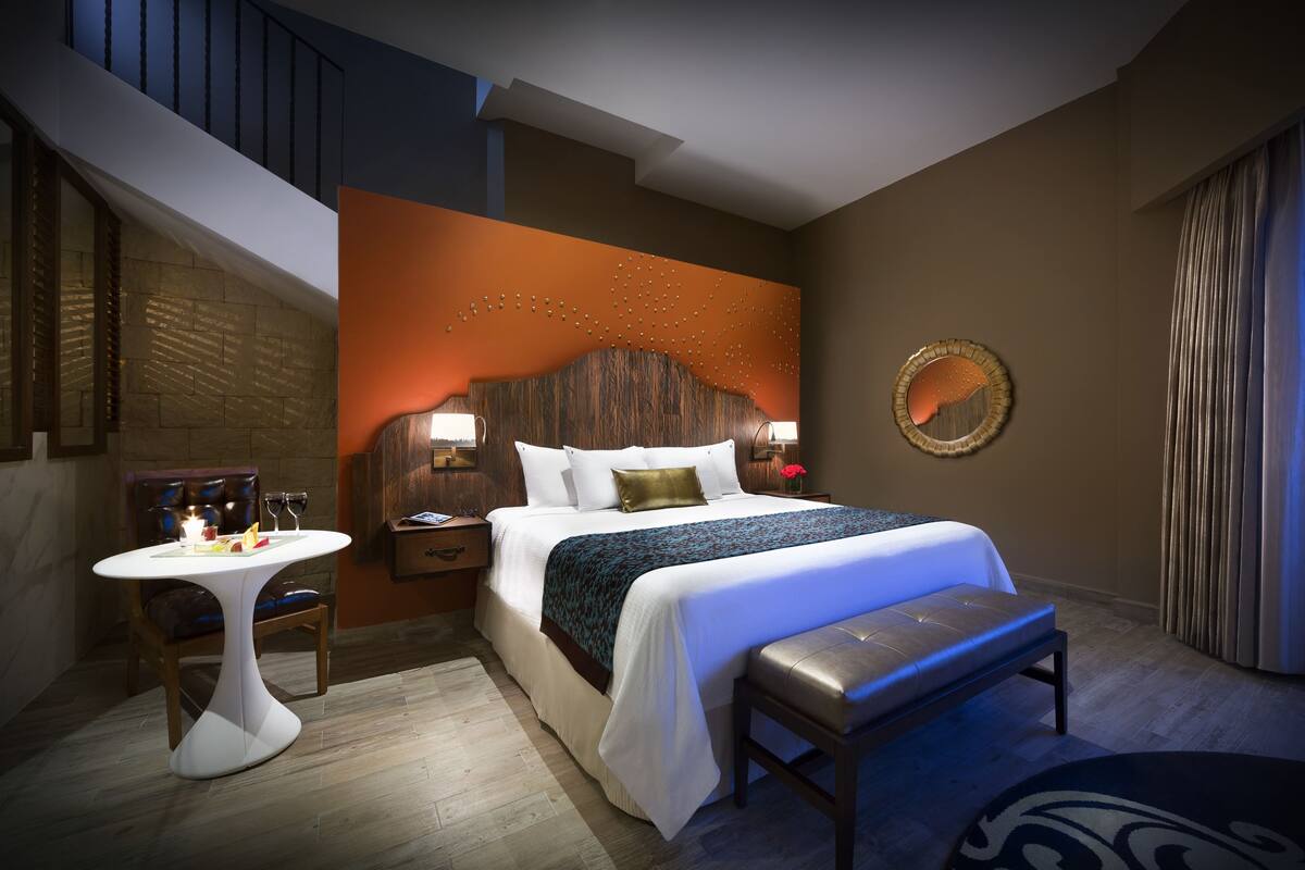 A hotel room with a bed, bedside table, bench, and a dining table.