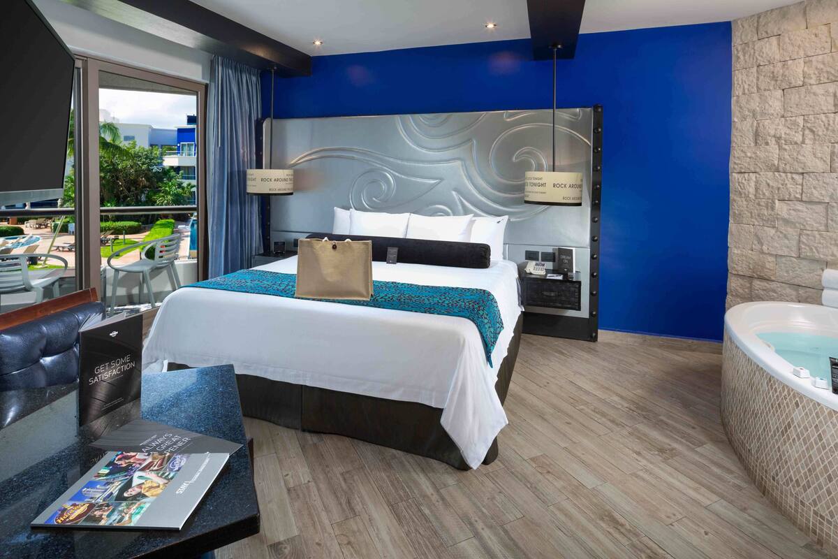 A modern hotel room with a large bed, a desk, a laptop, and a view of the outdoor area.