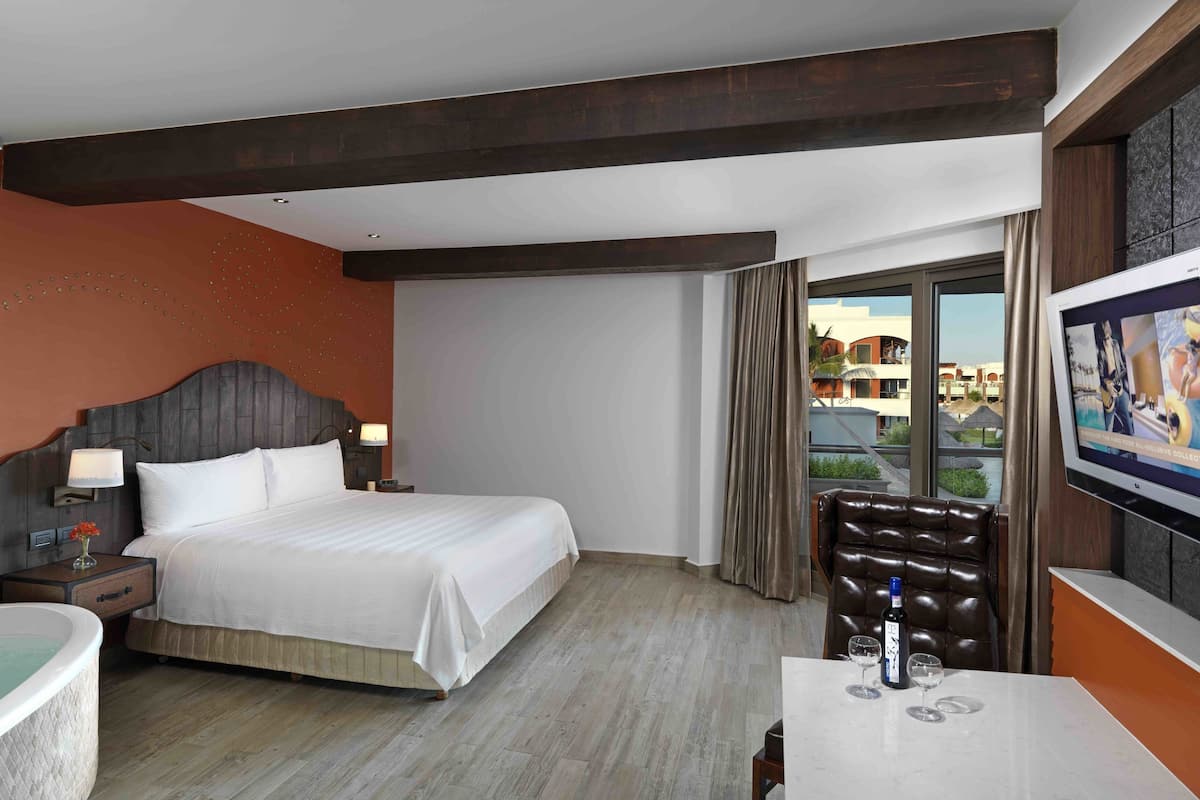A hotel room with a large bed, a TV, a seating area, and a view of buildings outside.