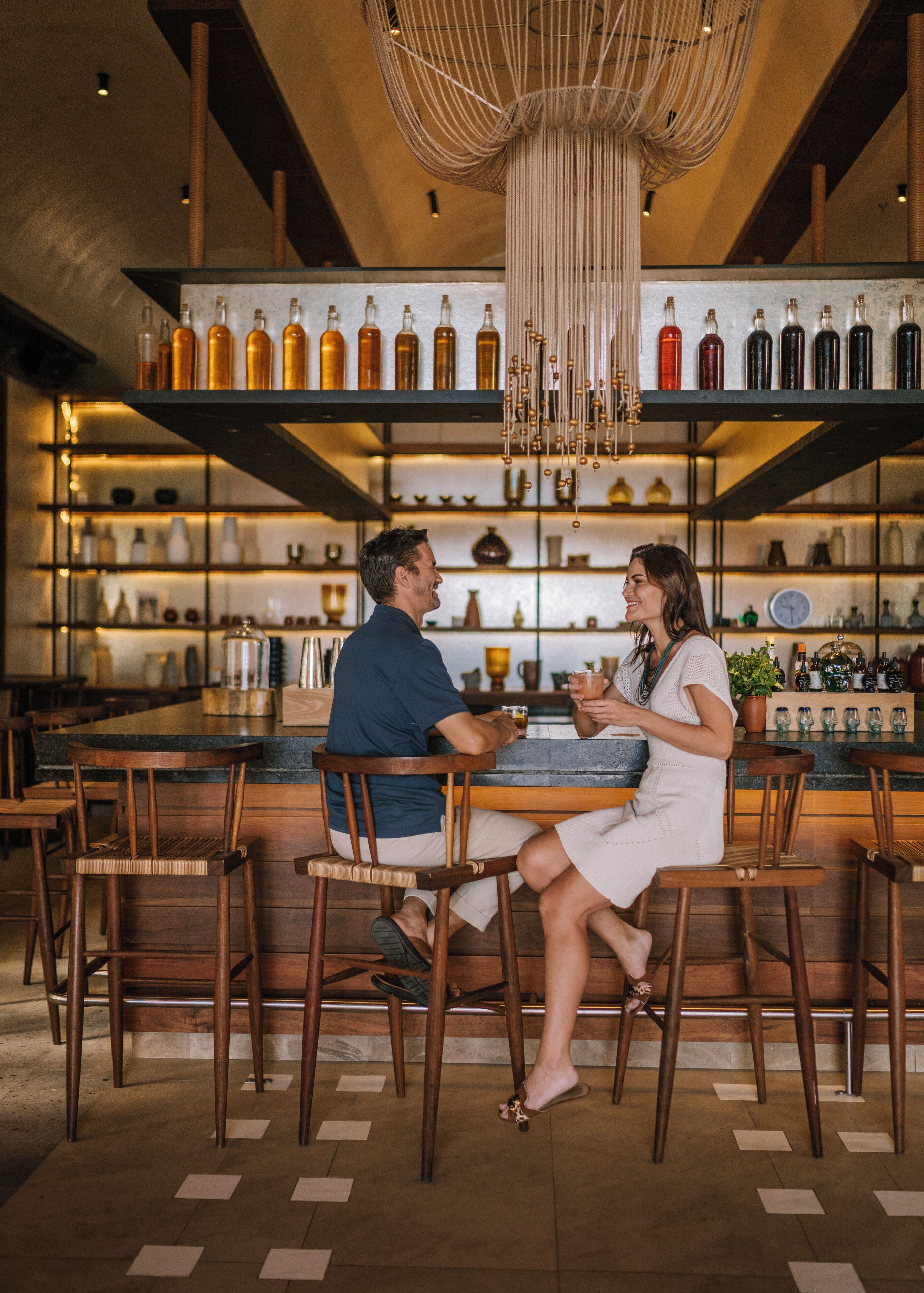 Una pareja sentada en un bar, con una variedad de botellas y vasos en las estanterías de fondo.