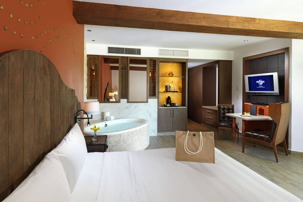 A modern hotel room with a large bed, a bathtub, a dining area, and a TV.