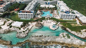An aerial view of a resort with multiple buildings, a central pool area, and surrounding rocky coastline. - Hard Rock Hotel Riviera Maya -  All Inclusive (Puerto Aventuras)