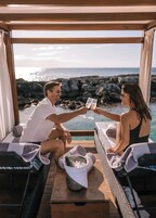 Una pareja brindando con copas de champán en una zona de estar exterior acogedora con vistas al océano.