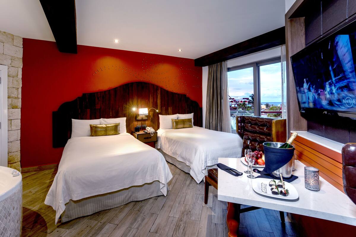 A hotel room with two beds, a TV, a table with a bottle of champagne, and a view of the city.