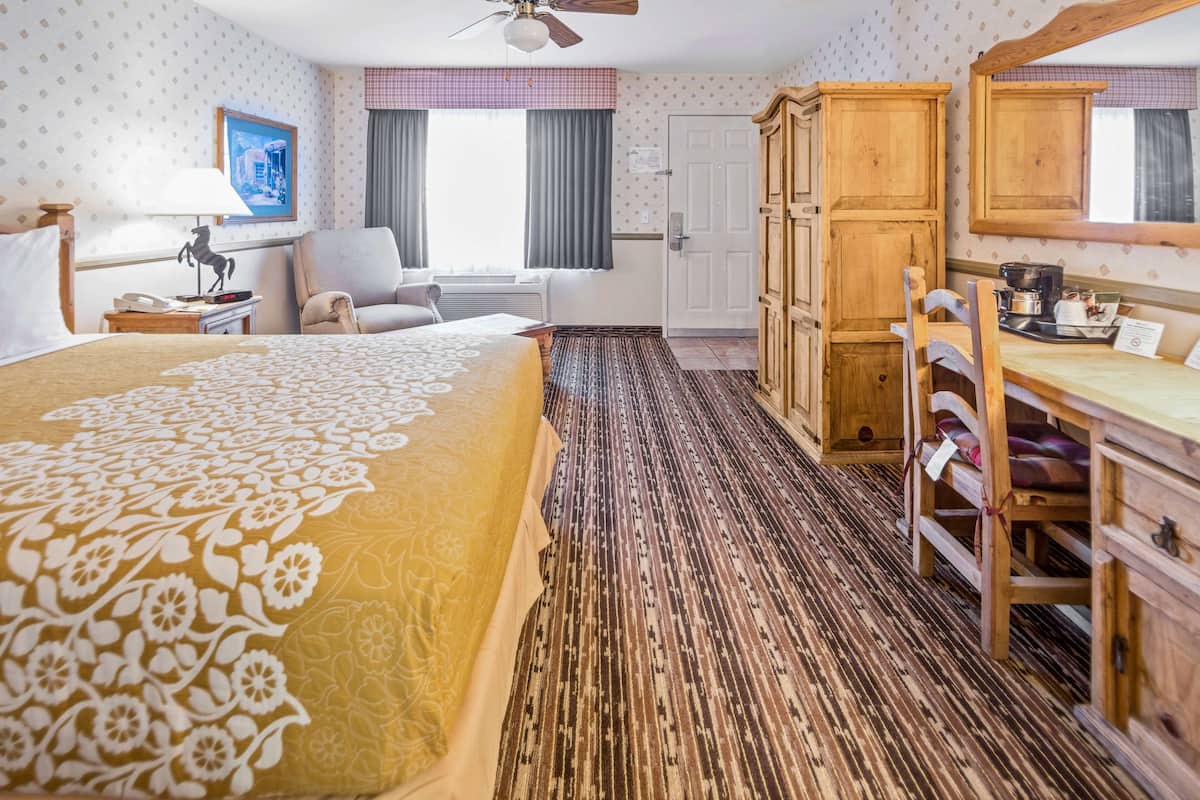 A hotel room with a large bed, a desk, a chair, a wardrobe, and a window with curtains.