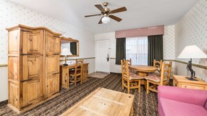 A room with a wooden wardrobe, a dining table with chairs, a pink sofa, and a ceiling fan. - Days Inn by Wyndham Lebec (Lebec)