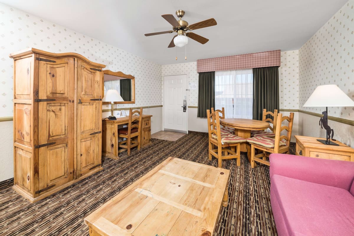 A room with a wooden wardrobe, a dining table with chairs, a pink sofa, and a ceiling fan.