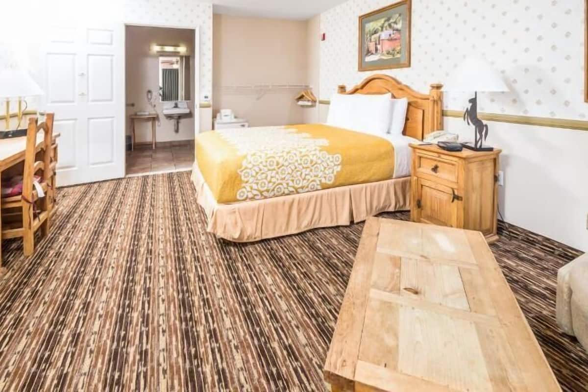 A hotel room with a bed, bedside table, wooden desk, chair, and a small table.