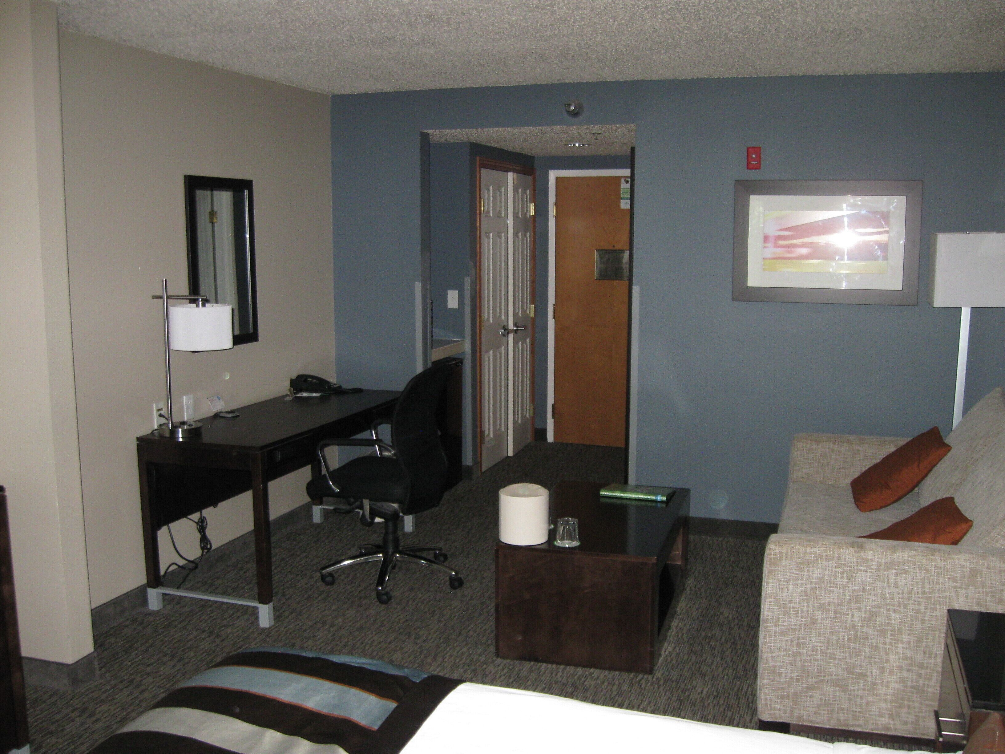 A hotel room with a bed, a desk, a chair, a coffee table, and a couch.
