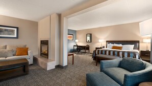 Ein Hotelzimmer mit einer Couch, einem Sessel, einem Schreibtisch, einem Bett und einem Kamin.