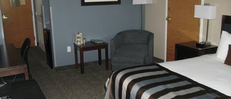 A hotel room with a bed, a desk, a chair, a small table with a coffee maker, and a framed picture on the wall.