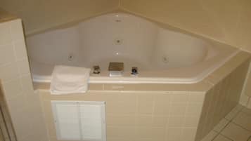 A bathroom with a corner bathtub, a towel, and a window with blinds.