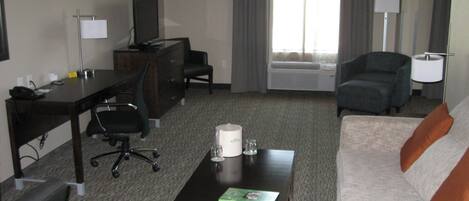 A hotel room with a desk, office chair, sofa, and a coffee table.