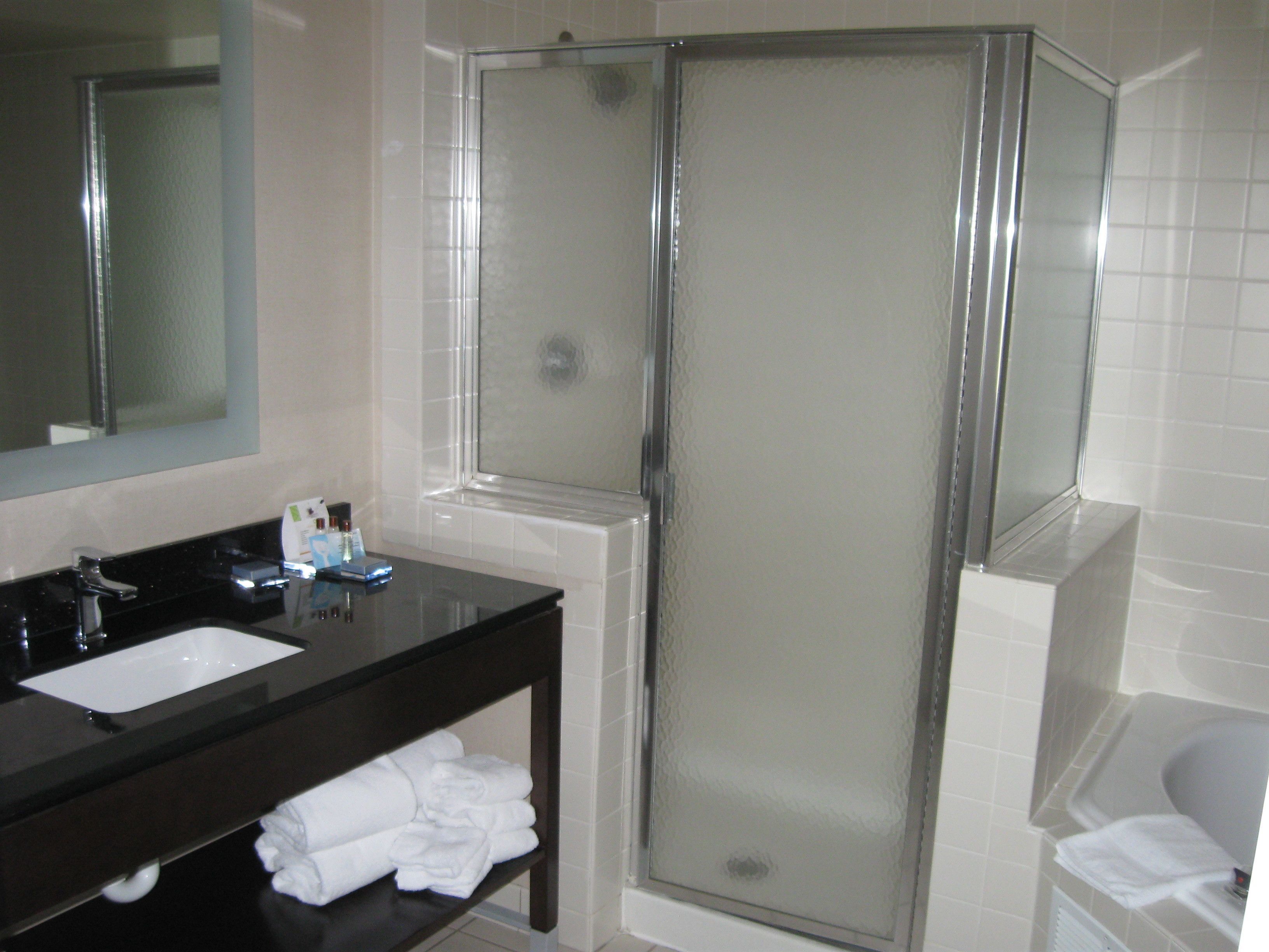 A bathroom with a black vanity, a white sink, a mirror, a glass shower enclosure, and a white bathtub.