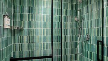 Un baño con baldosas verdes a rayas, ducha con cabezal de ducha manual y dispensador de jabón en la pared.
