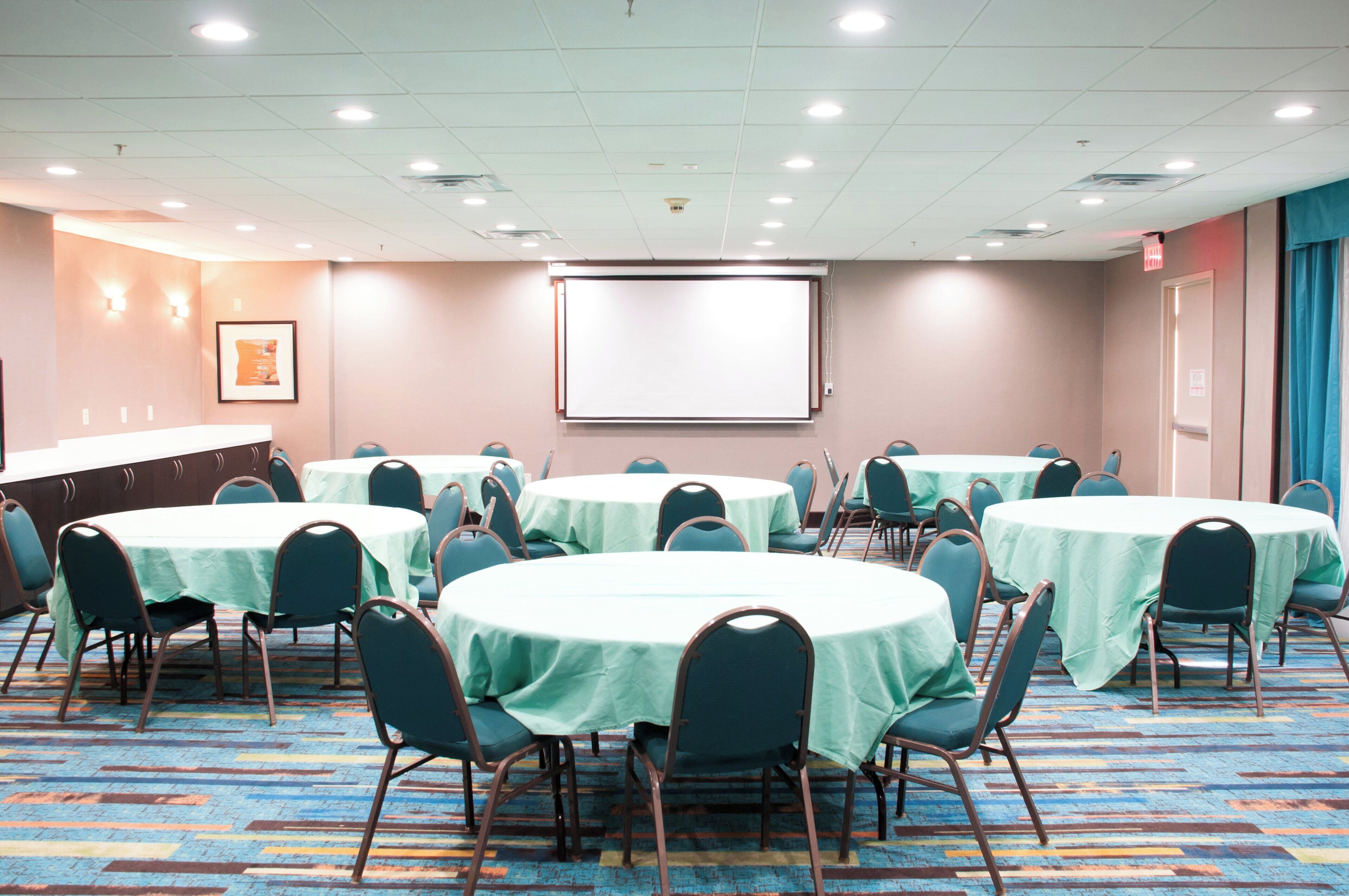 Una sala conferenze con diversi tavoli e sedie, uno schermo per proiettore e uno schermo per presentazioni.