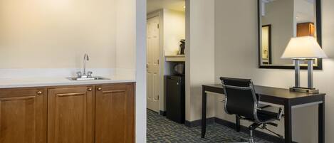 A hotel room with a wooden cabinet, a desk with a chair, a mirror, and a lamp.