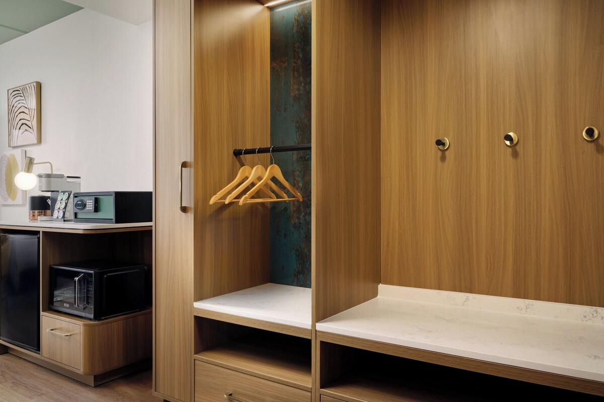 A wooden wardrobe with a hanging rack, a microwave, and a coffee machine on a shelf.