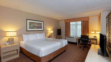 A hotel room with a large bed, bedside tables with lamps, a desk with a chair, a television, and a window with curtains.
