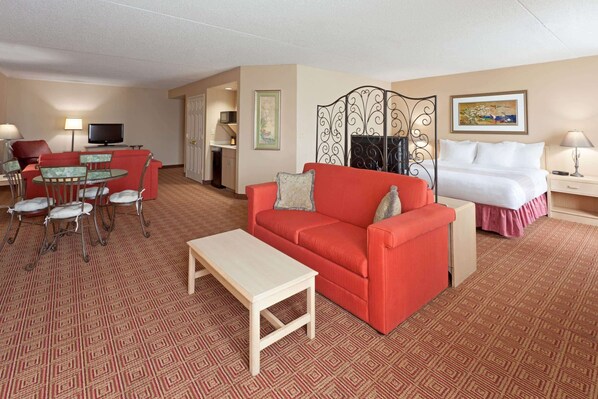 A hotel room with a red sofa, a small table, a TV, a bed, and a decorative screen.