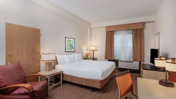 A hotel room with a bed, two chairs, a desk, a television, and a window with curtains.