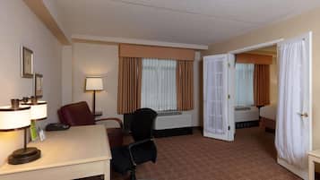 A hotel room with a desk, chair, bed, and an open door leading to another room.