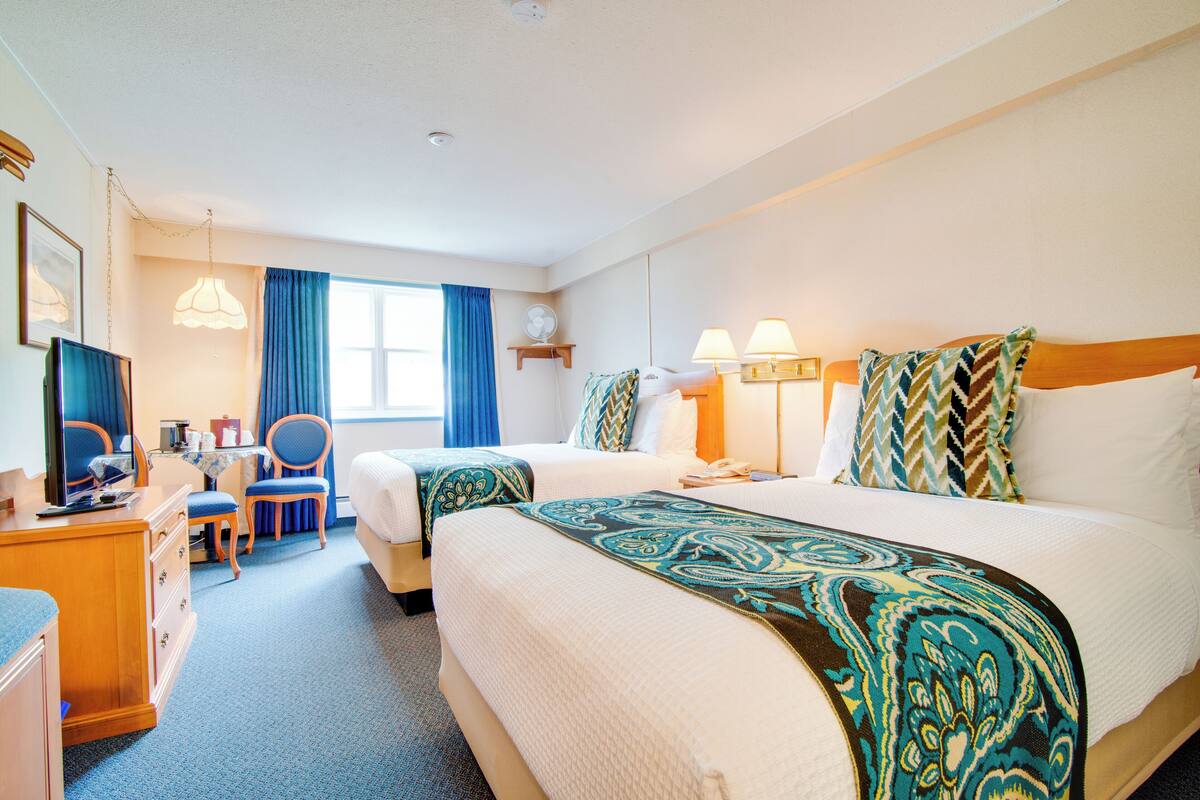 A hotel room with two beds, a desk, a chair, a television, and a window with curtains.