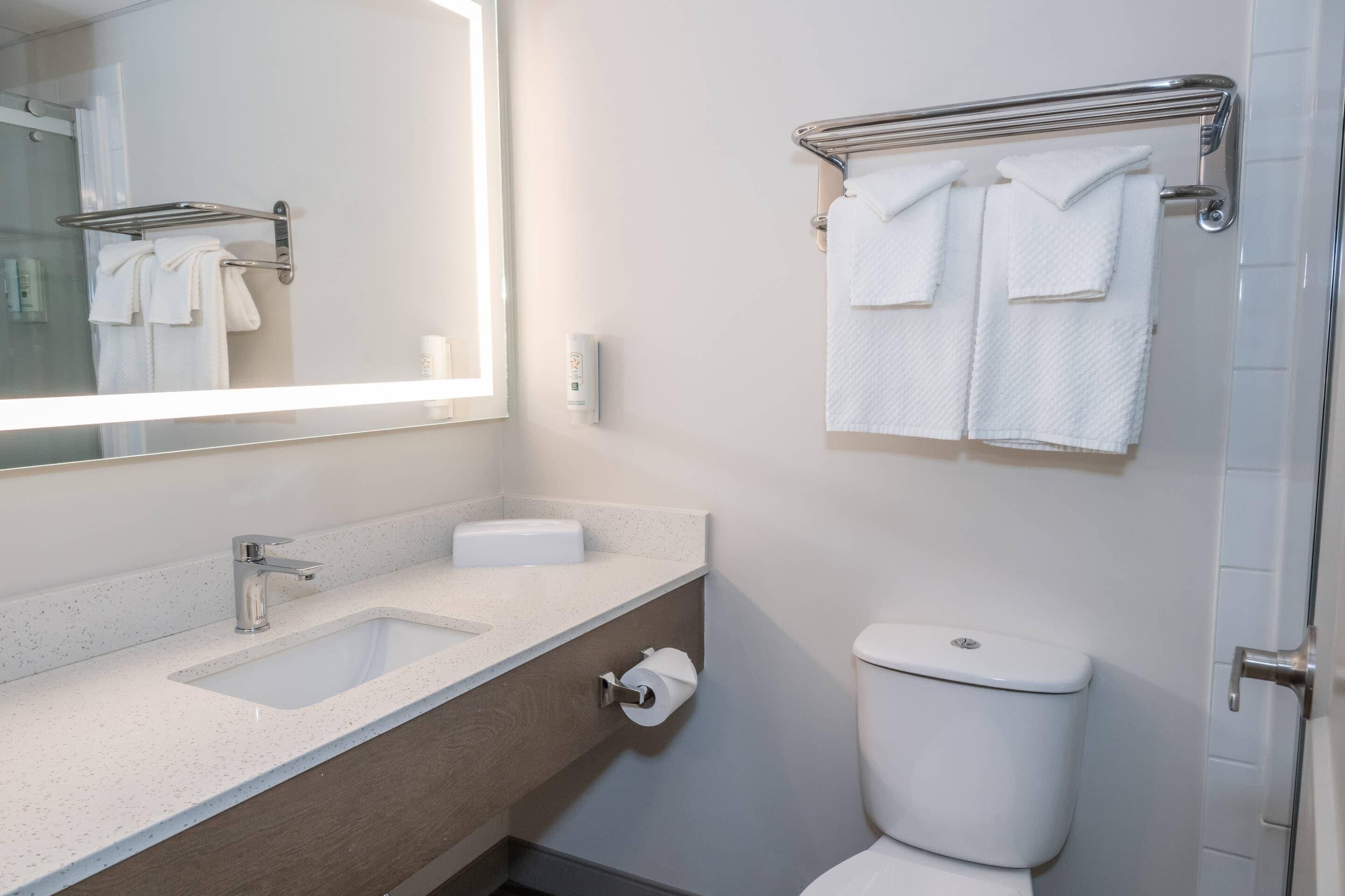 A modern bathroom with a white sink, a mirror, a toilet, and a towel rack.