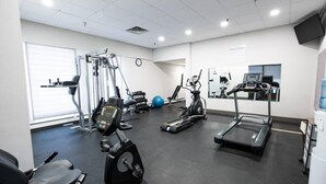 Een sportschool met cardioapparatuur, gewichten en een spiegelwand.