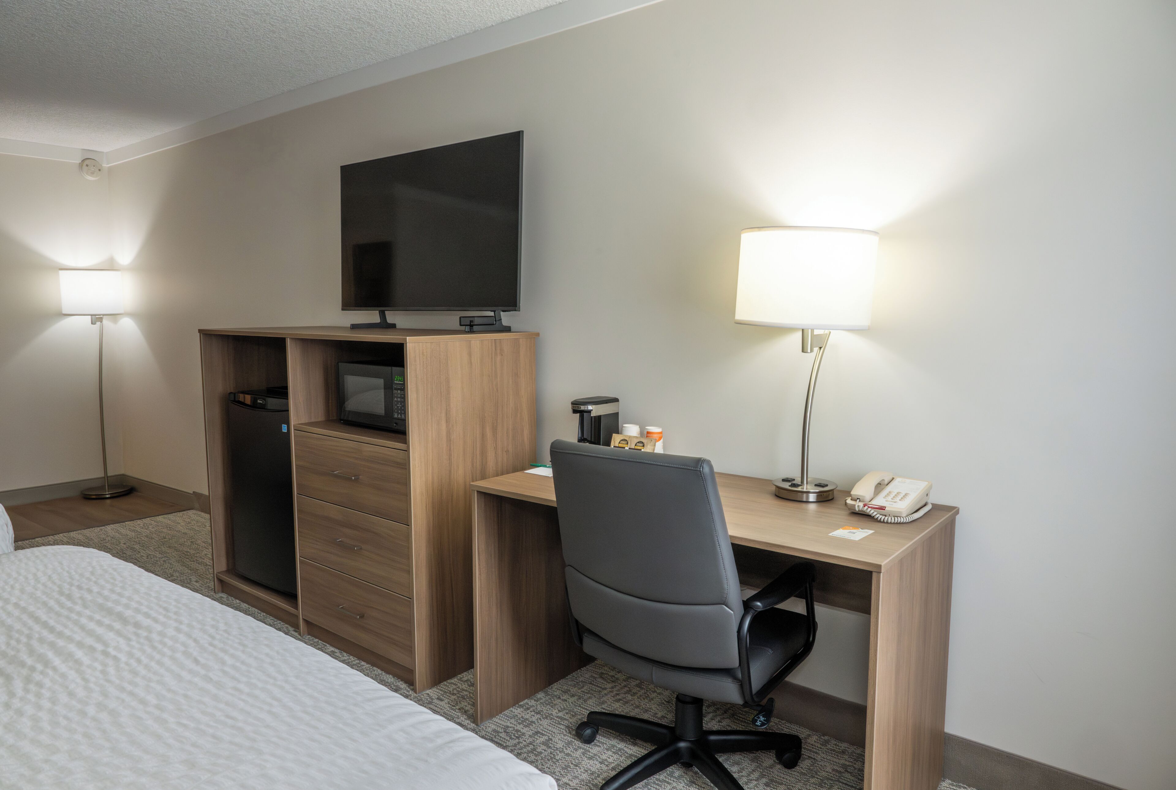 Une chambre d’hôtel comprenant un lit, un bureau avec une chaise, une télévision, une lampe de bureau et un téléphone.