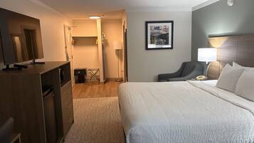 Une chambre d’hôtel avec un lit, un bureau, une chaise, une télévision et un tableau encadré au mur.