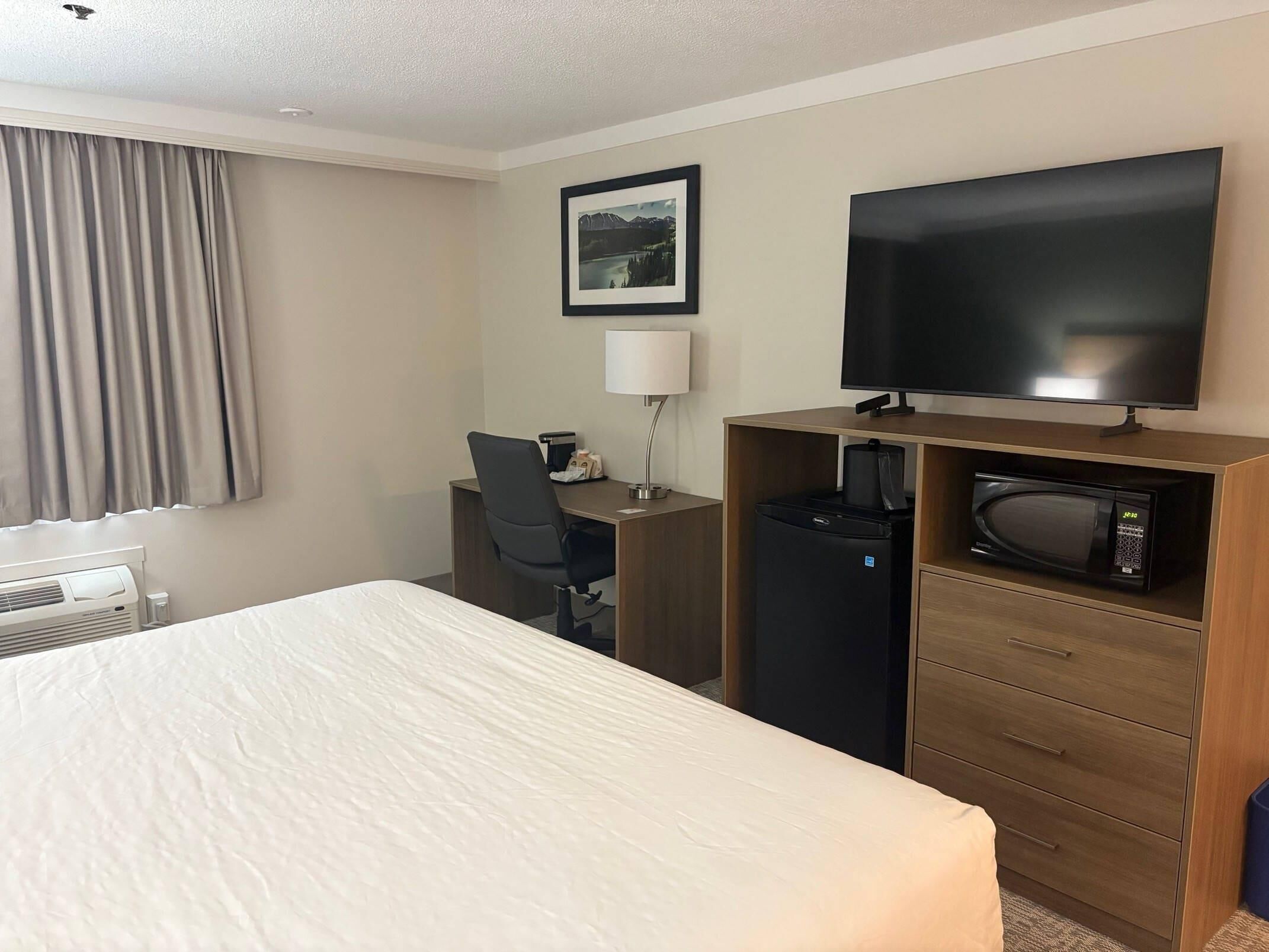 A hotel room with a bed, a desk with a chair, a television, a microwave, and a coffee maker.