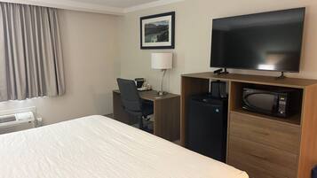 A hotel room with a bed, a desk with a chair, a television, a microwave, and a coffee maker.