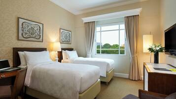 A hotel room with two beds, a desk, a TV, and a window with curtains.