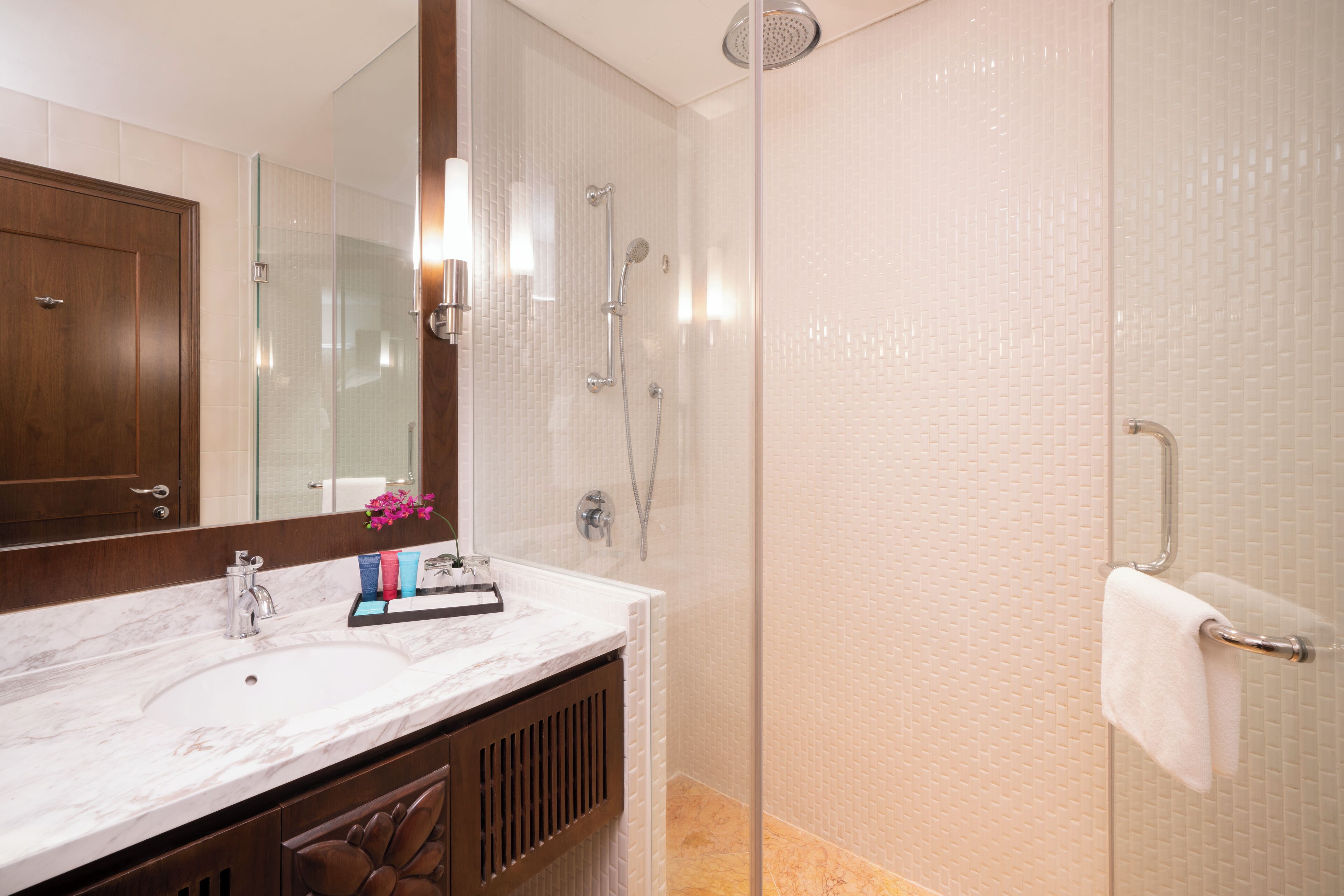 Un baño moderno con lavamanos de mármol, ducha con cerramiento de vidrio y tocador de madera.