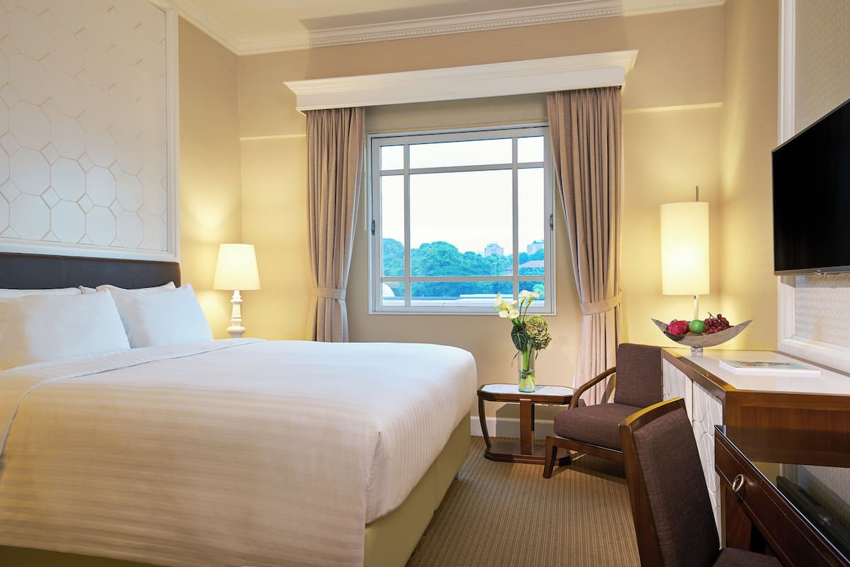 A hotel room with a large bed, a desk with a TV, a chair, a lamp, and a window with curtains.