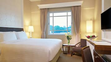 A hotel room with a large bed, a desk with a TV, a chair, a lamp, and a window with curtains.