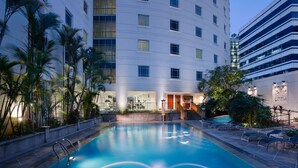 A swimming pool with a fountain, surrounded by palm trees and a modern building with multiple floors and balconies. - Rendezvous Hotel Singapore by Far East Hospitality (Singapore)