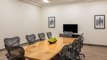A conference room with a wooden table, black mesh chairs, a bowl of green plants, and two framed pictures on the walls.