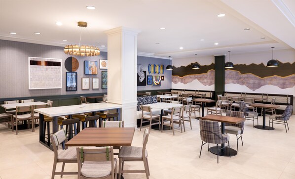 A modern restaurant interior with multiple dining tables and chairs, a large chandelier, and various artworks on the walls. - Hilton Garden Inn Denver Tech Center (Denver)
