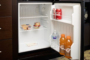 Un refrigerador con estantes que contienen una lata de Coca-Cola, dos botellas de jugo de naranja, una botella de agua y dos recipientes de yogur.